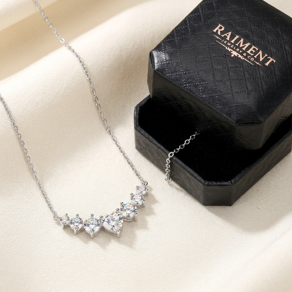 Raiment Jewelry & Co. moissanite graduated cluster necklace beside open jewelry box on cream background
