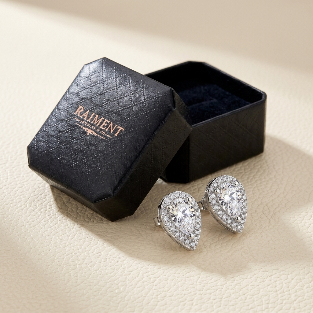 Moissanite pear halo stud earrings styled beside jewelry box on cream, Raiment Jewelry & Co.
