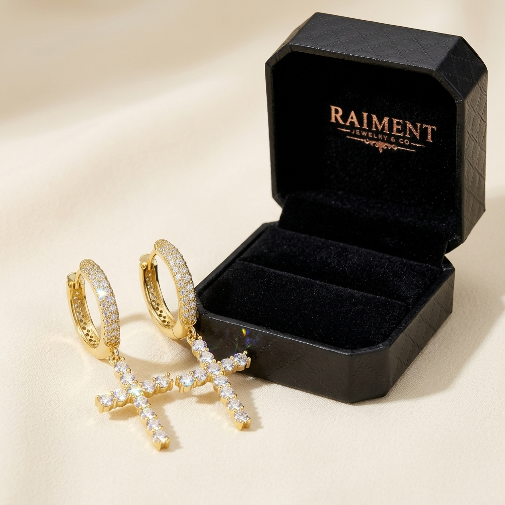 Raiment Jewelry & Co. moissanite cross huggie earrings beside open jewelry box on cream background