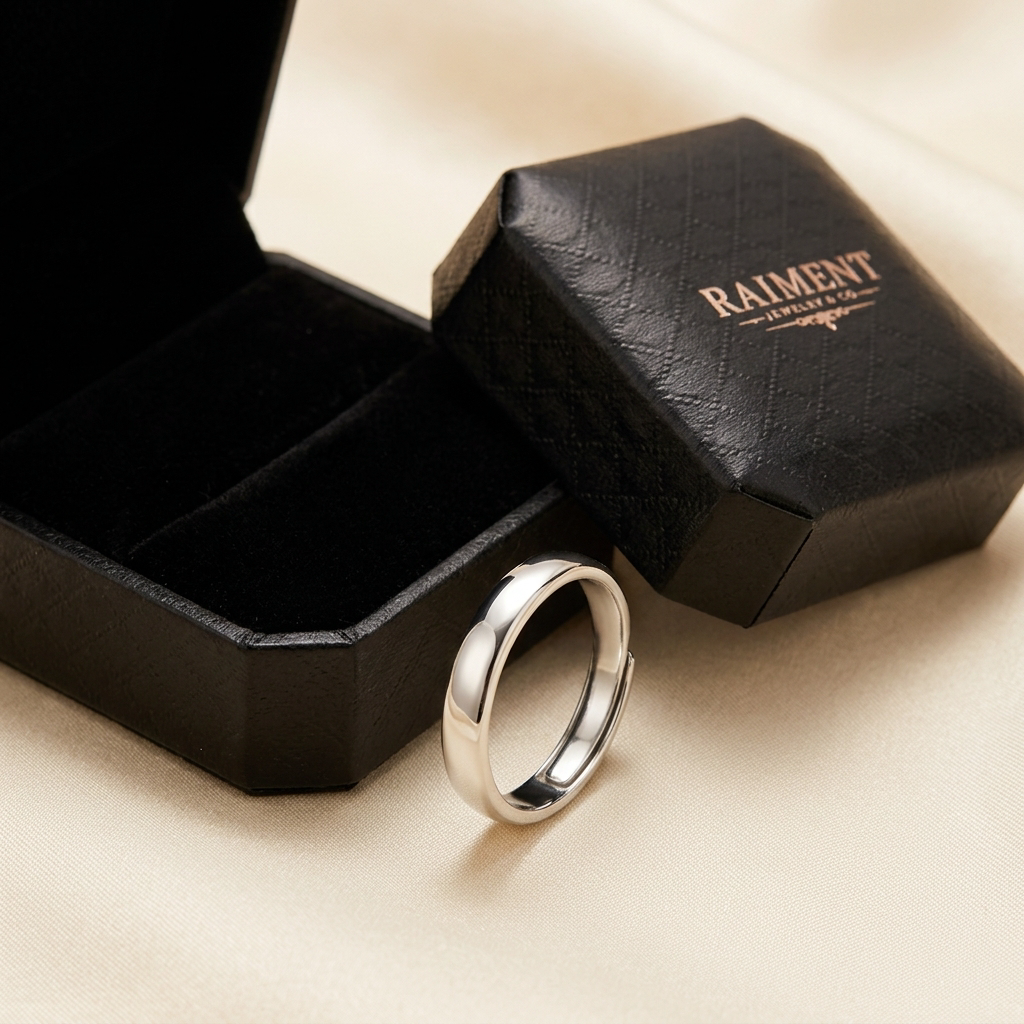 Men's polished band ring styled beside jewelry box on cream, Raiment Jewelry & Co.